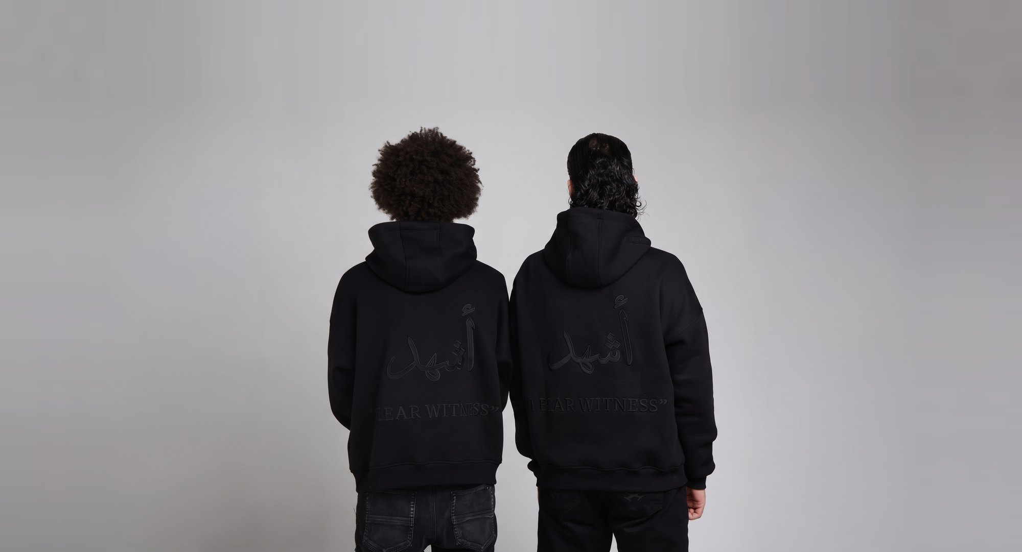 Ash-Hadu — two models in black hoodies showing the أشهد 'I bear witness' back print